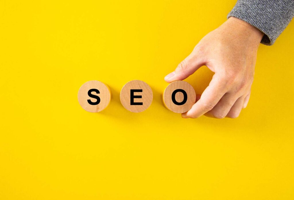 Hand arranging wooden blocks spelling SEO on yellow background, representing Affordable SEO Company in London.