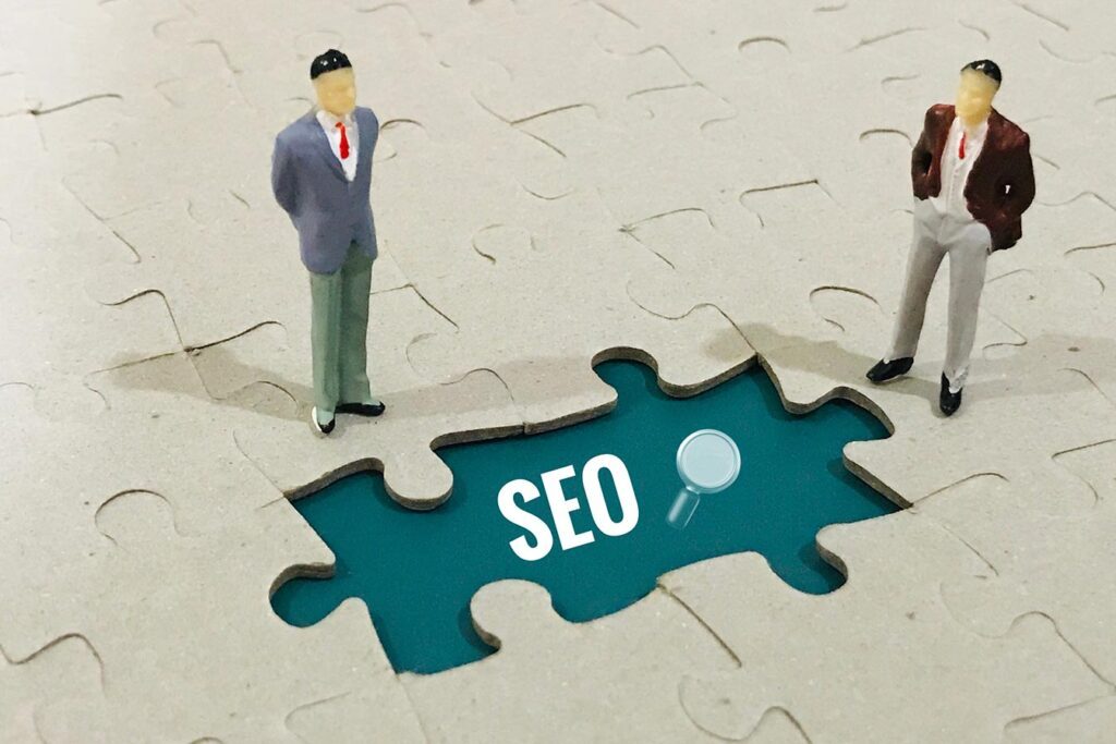 Miniature figures on a puzzle with a missing piece revealing "SEO," symbolizing link building strategies.