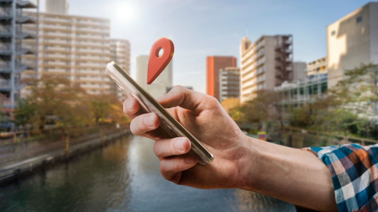 Hand holding phone with location pin, symbolizing Local SEO Services in London, set against a cityscape background.