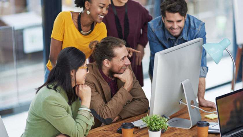 Team collaborating at a web development company in London, gathered around a computer in a bright office space.