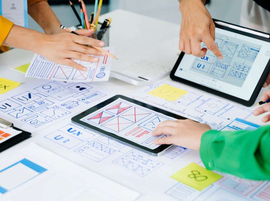 Team collaborates on website design, using tablets and paper layouts, highlighting how aesthetics influence user choices.